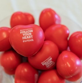 A clear glass bowl holds red stress relievers shaped like hearts that read "Follow your heart at SUNY Adirondack"