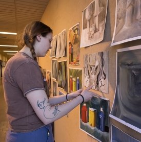 SUNY Adirondack Fine Arts student Mackenzie Spencer hangs artwork on a bulletin board in the hallway of Dearlove Hall