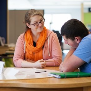 Two people lean over papers together, working on a writing assignment