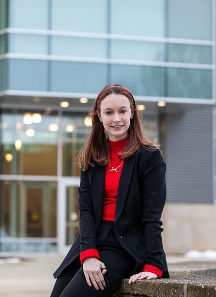 Abigail Saunders sits on a stone wall outside Adirondack Hall on the SUNY Adirondack Queensbury campus