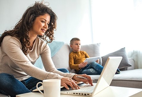 Woman logging onto her computer with her young son in the background