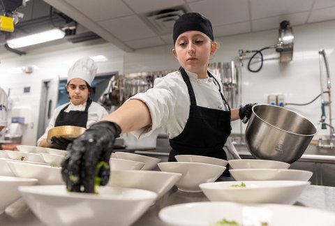 A Culinary student places salad greens on a counter full of bowls