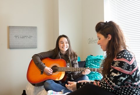 A student plays guitar on her bed in the Residence Hall