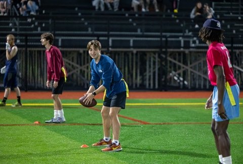 Students and onlookers preparing to start a game of flag football on the turf