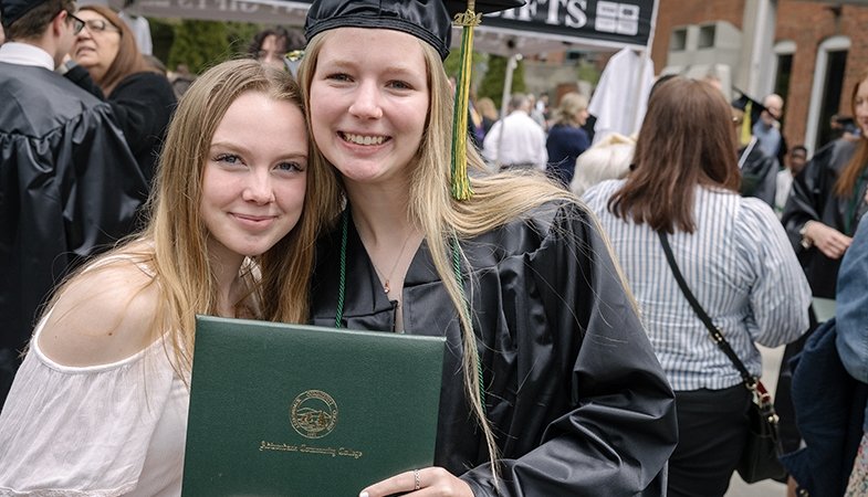 A graduate poses for a photograph with a friend outside Cool Insuring Arena